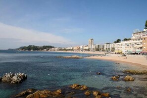 A coastal cityscape with a beach, rocky shoreline, and buildings along the waterfront.