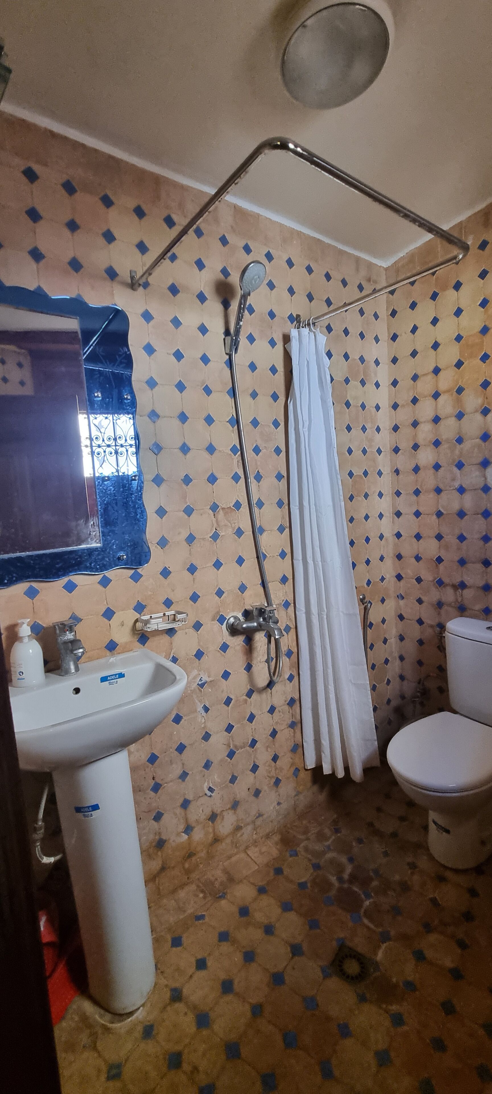 A bathroom with a tiled floor, a white sink, a toilet, and a shower with a curtain.