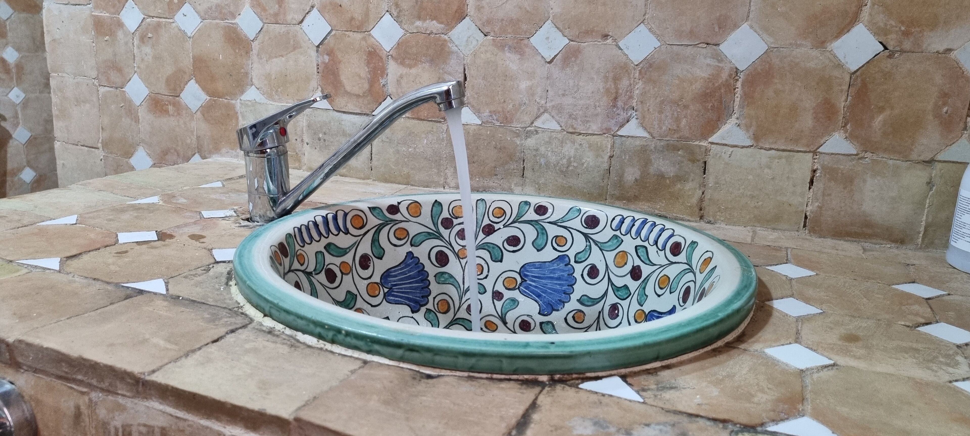 A ceramic sink with a decorative pattern, mounted on a tiled countertop.