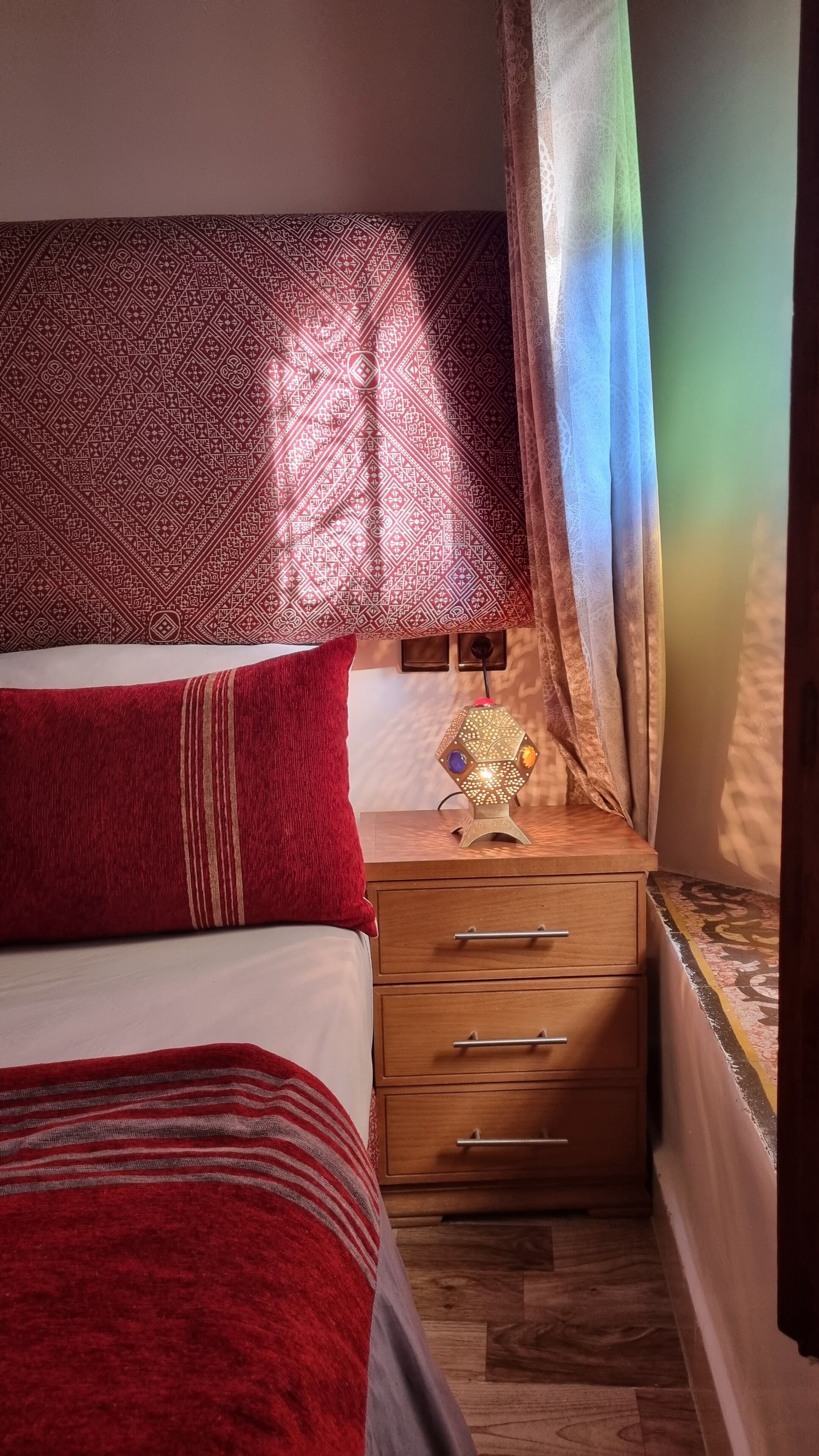 A bedroom with a bed, a bedside table with a lamp, and a window with curtains.