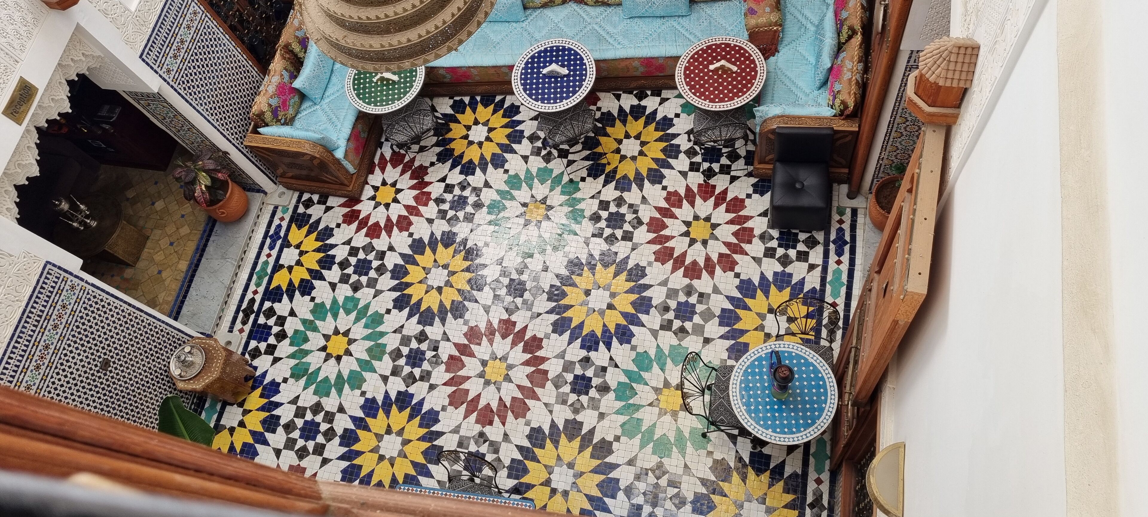 A Moroccan interior with a colorful mosaic floor, a wooden table with a blue and white patterned top, and a traditional hanging lamp.
