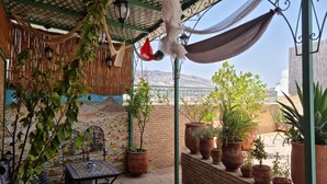 A covered patio with a hammock, potted plants, a table with a decorative bowl, and a mural on the wall. - Fes Touria Palace (Fes)