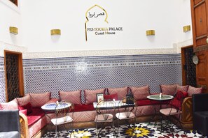A Moroccan-style guest house with patterned tile walls, a sofa set, and a small dining area. - Fes Touria Palace (Fes)
