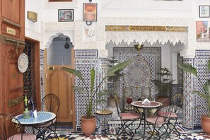 A Moroccan-style interior with a wooden door, tiled walls, and a dining area with a table and chairs. - Fes Touria Palace (Fes)