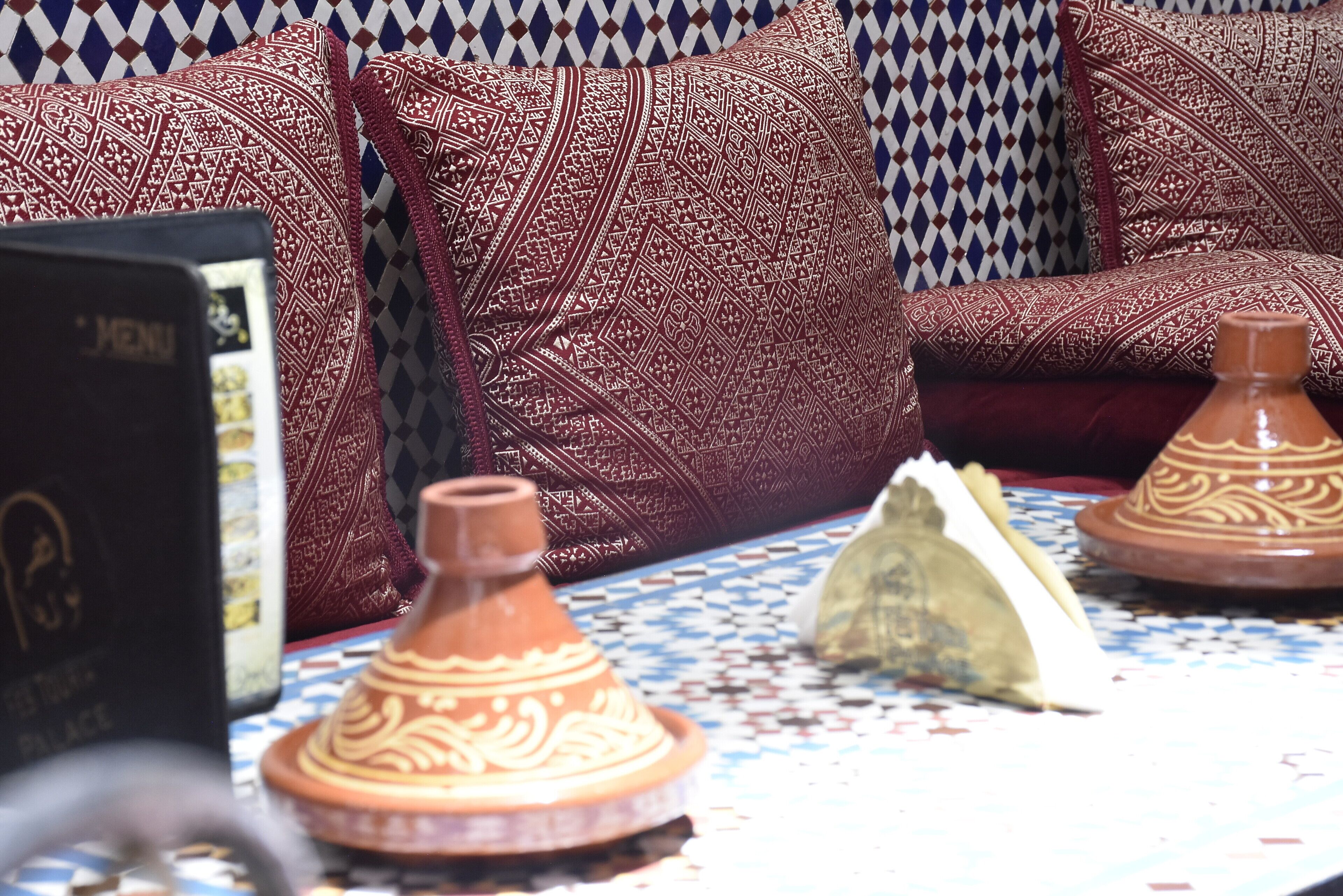 A Moroccan-style sofa with intricate red and white patterns, a traditional Moroccan tagine, and a patterned tablecloth.