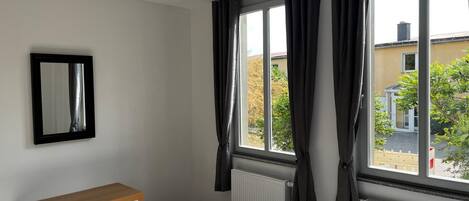 Ein Schlafzimmer mit einem Holzkasten, einem Bett, einem Heizkörper und einem Fenster mit Vorhängen.