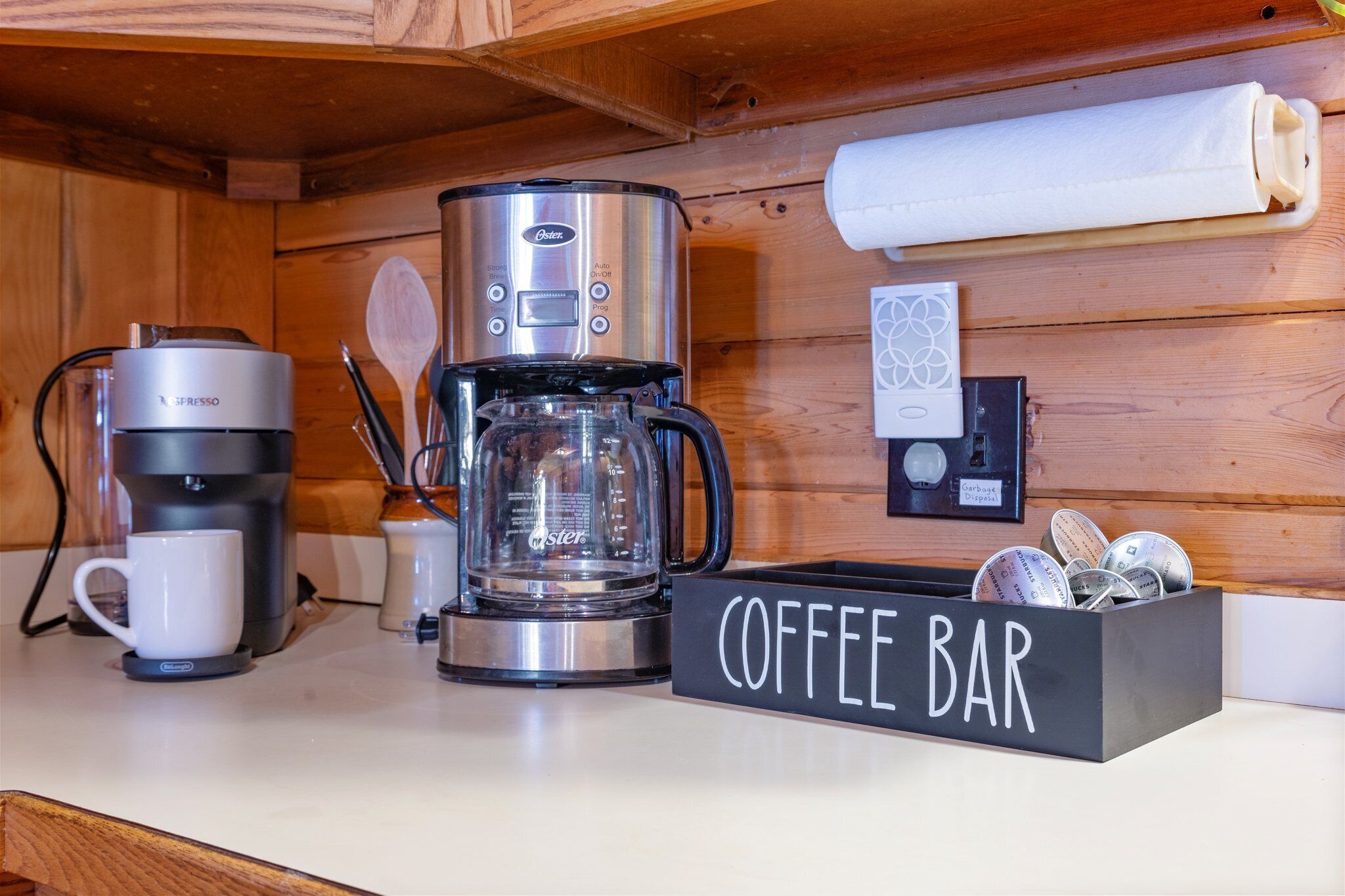 A coffee station with a coffee maker, a glass carafe, a coffee mug, and a coffee bar sign.