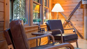 A wooden cabin interior with a leather chair, a small table, a lamp, and a large axe leaning against the wall. - Lake front, hot tub, kayak, paddle board, Dogs, Mount Desert Island, Bar Harbor! (Mariaville)