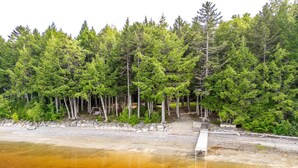 A forested area with a wooden dock extending into a body of water. - Lake front, hot tub, kayak, paddle board, Dogs, Mount Desert Island, Bar Harbor! (Mariaville)