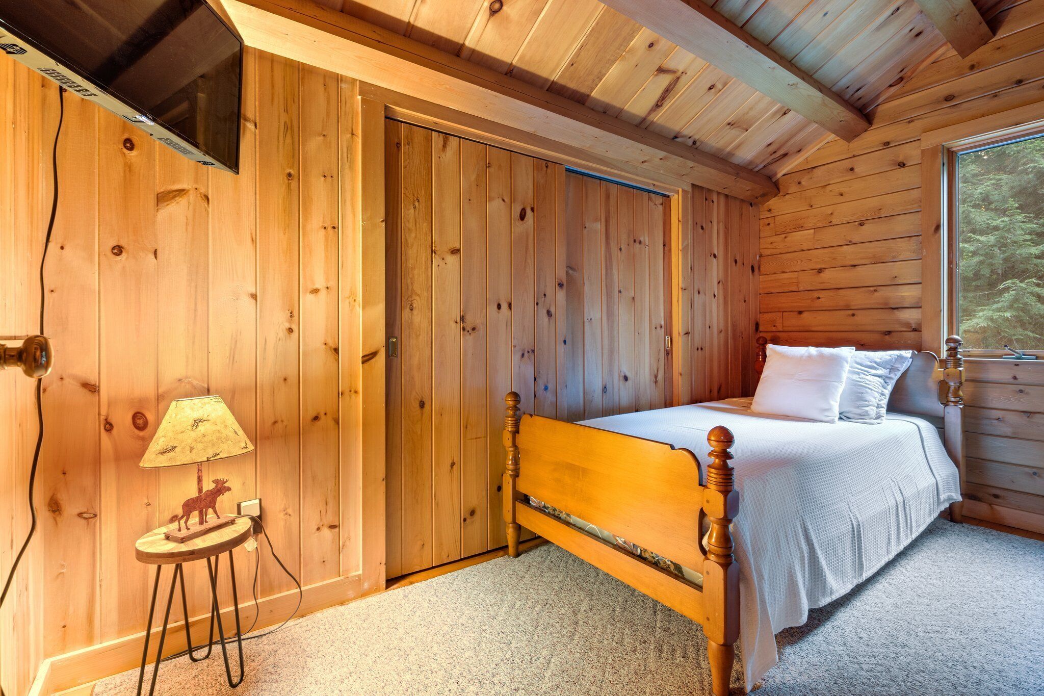 A wooden room with a bed, a lamp, and a small table with a moose figurine.