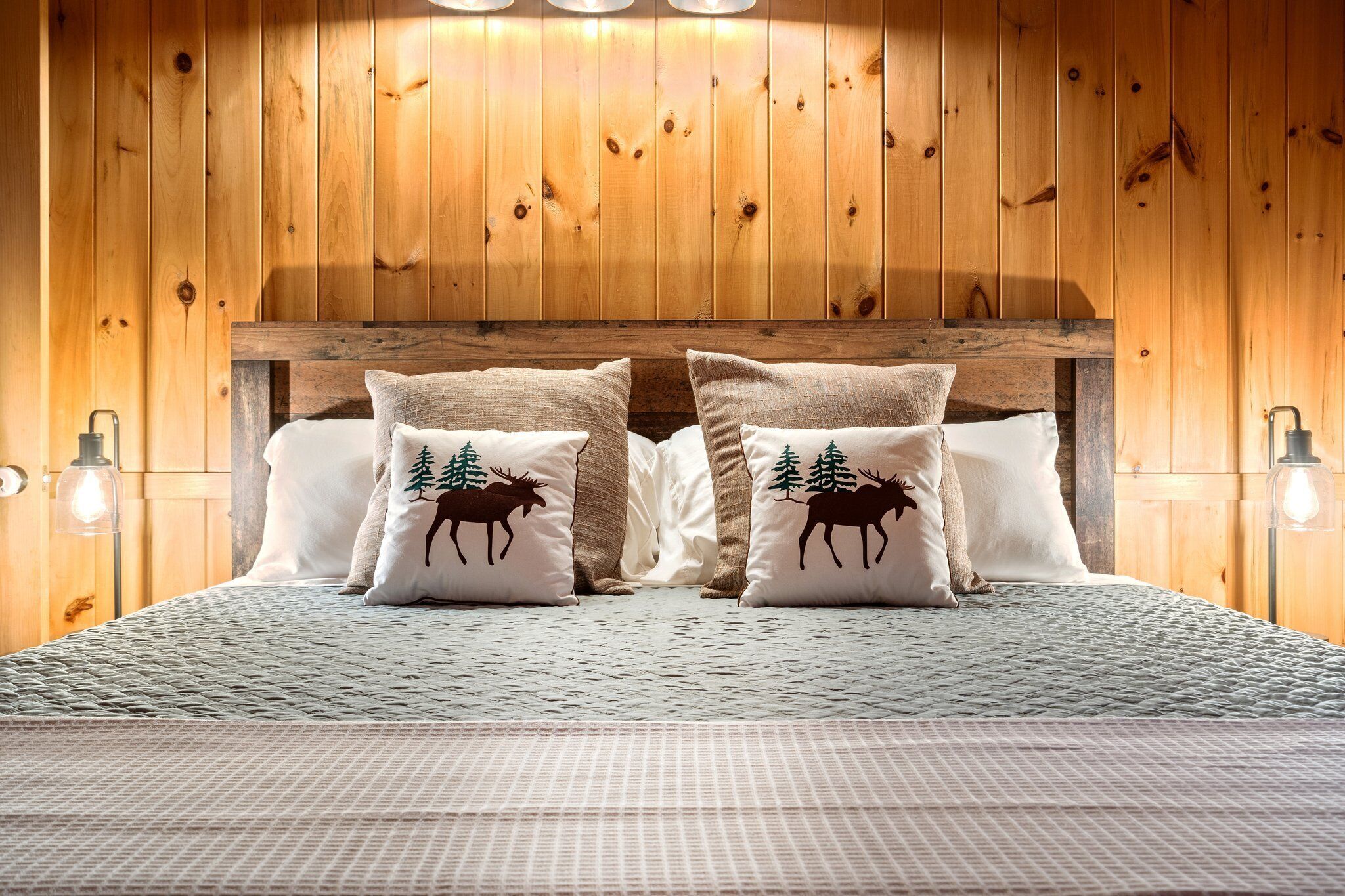 Un dormitorio con paneles de madera y una cama con dos almohadas decoradas con motivos de alce.