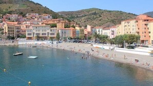 Une ville côtière avec des bâtiments le long du front de mer, une plage de sable et des bateaux sur l’eau.