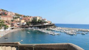 Une ville côtière dotée d’un port de plaisance, de bâtiments construits sur une colline et d’un ciel bleu azur.