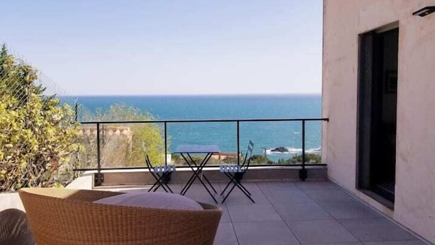 Un balcon avec vue sur l’océan, une chaise en osier et une table.