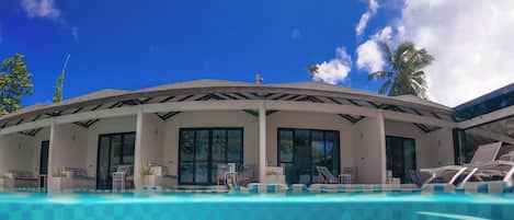A swimming pool with a checkered pattern, lounge chairs, and a covered area with large windows.