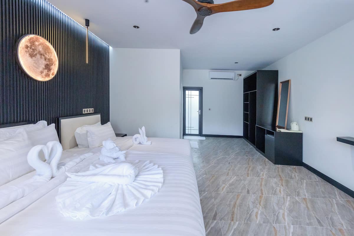 A modern hotel room with a large bed, a ceiling fan, a wall-mounted circular light, and a wardrobe.