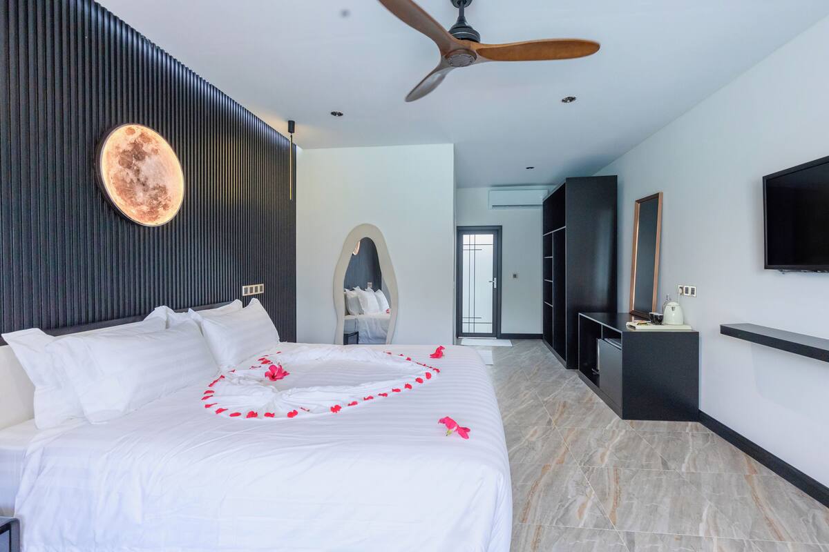 A modern hotel room with a large bed, a ceiling fan, a flat-screen TV, and a wardrobe.