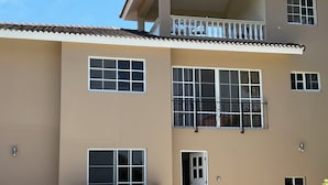 Un immeuble de deux étages doté d’un balcon, avec une voiture garée devant et une porte donnant sur l’entrée.