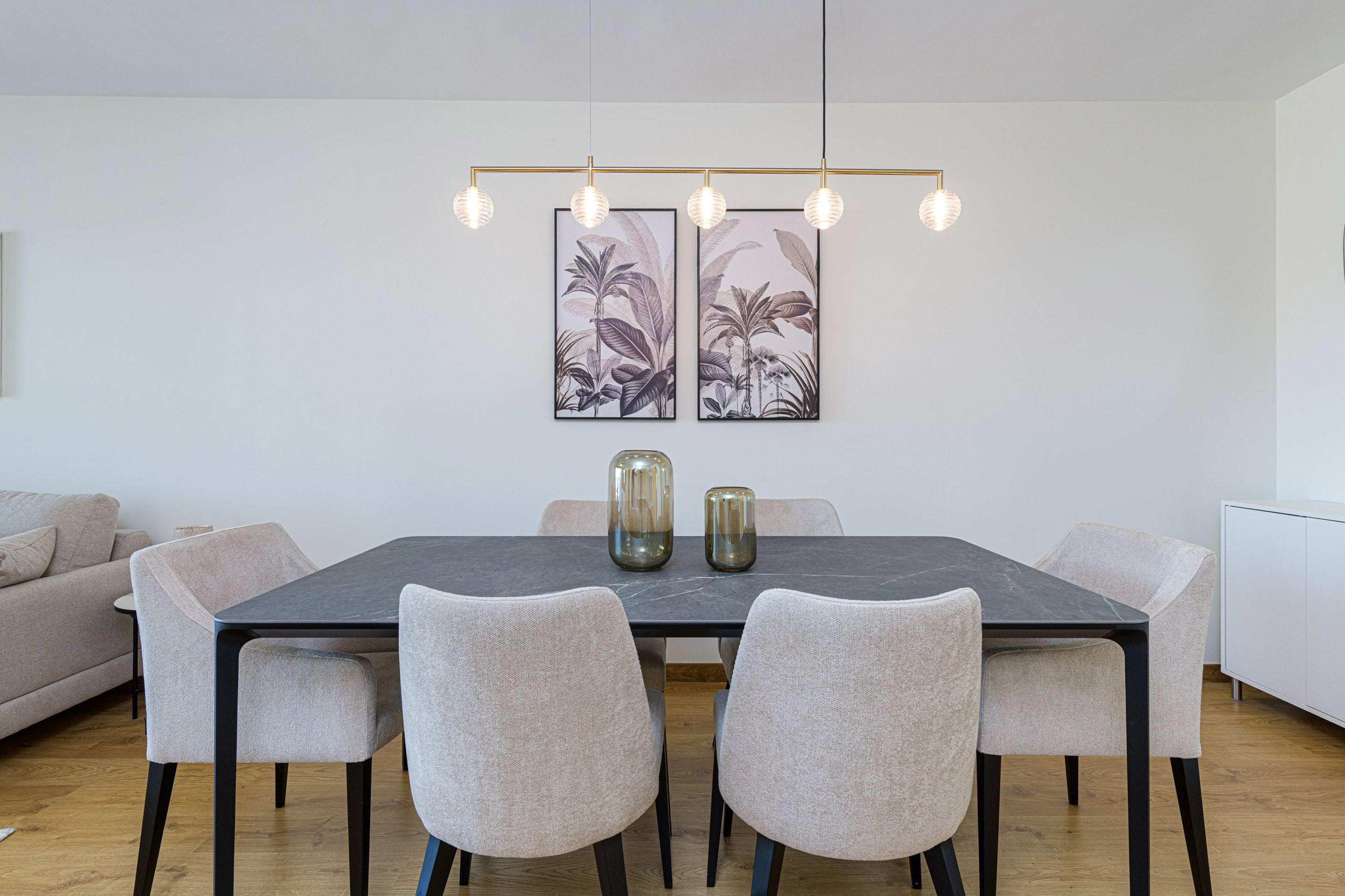 Ein Essbereich mit einem rechteckigen Tisch, vier Stühlen, einer Deckenleuchte und zwei an der Wand befestigten Bildern.