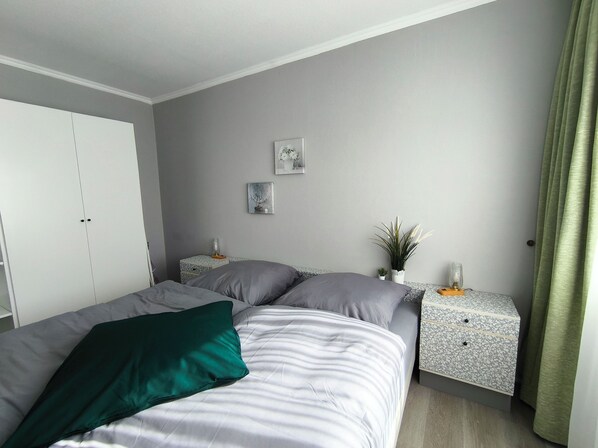 A bedroom with a bed, two nightstands, a wardrobe, and a green curtain.