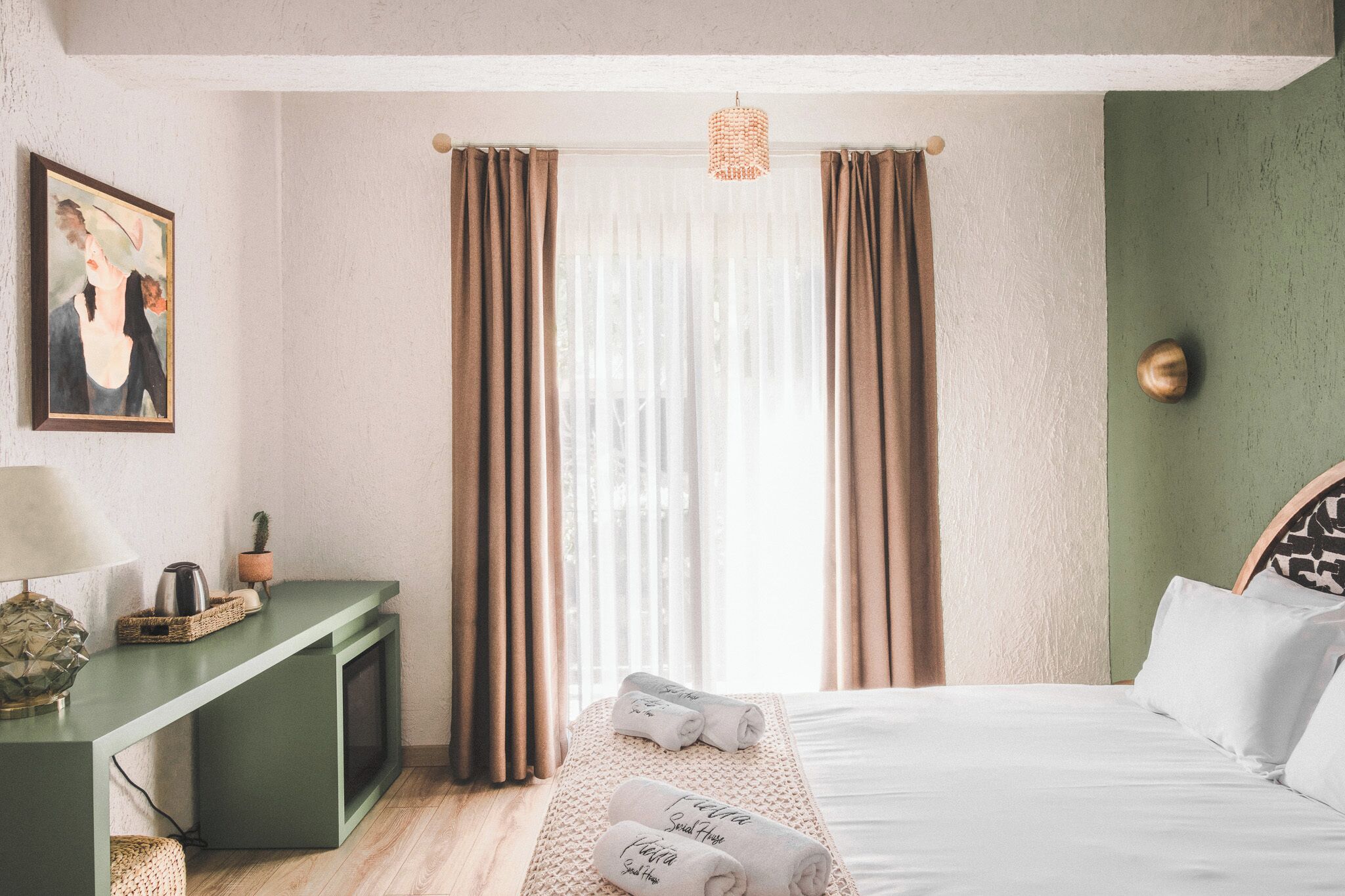 Een slaapkamer met een bed, een nachtkastje met een lamp, een schilderij aan de muur en een raam met gordijnen.