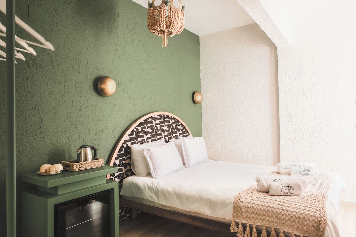 A neatly arranged bedroom with a green wall, a patterned headboard, and a bed with white linens.
