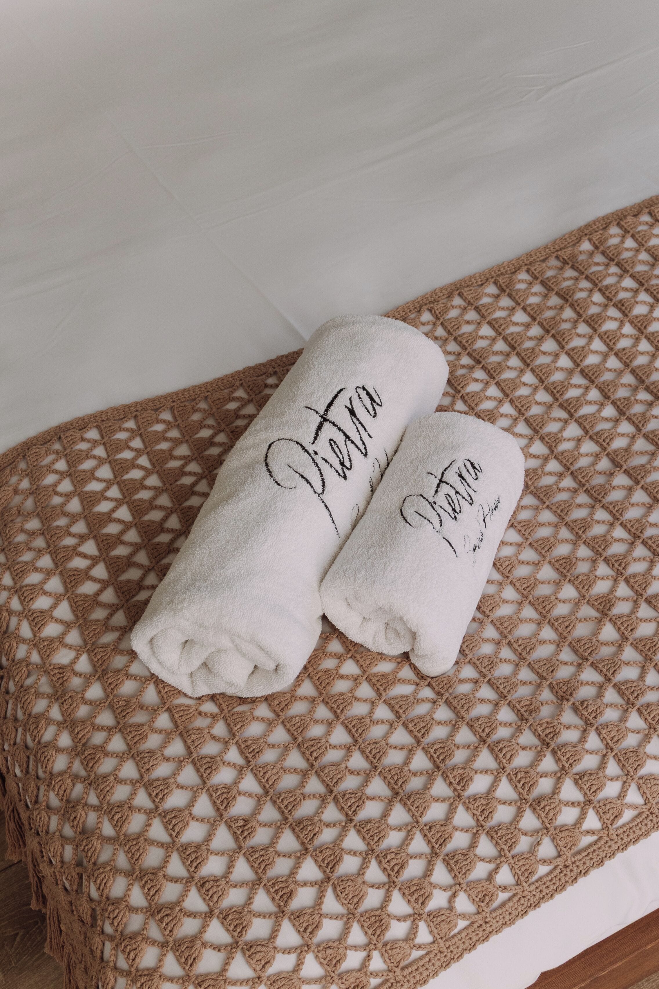 Two rolled towels with embroidered text on a woven bedspread.