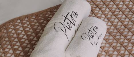 Two rolled towels with embroidered text on a woven bedspread.