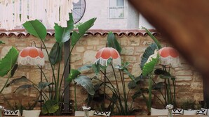 An outdoor patio area with wooden tables and chairs, large green plants, and a stone wall. - Pietra Social House (Urla)