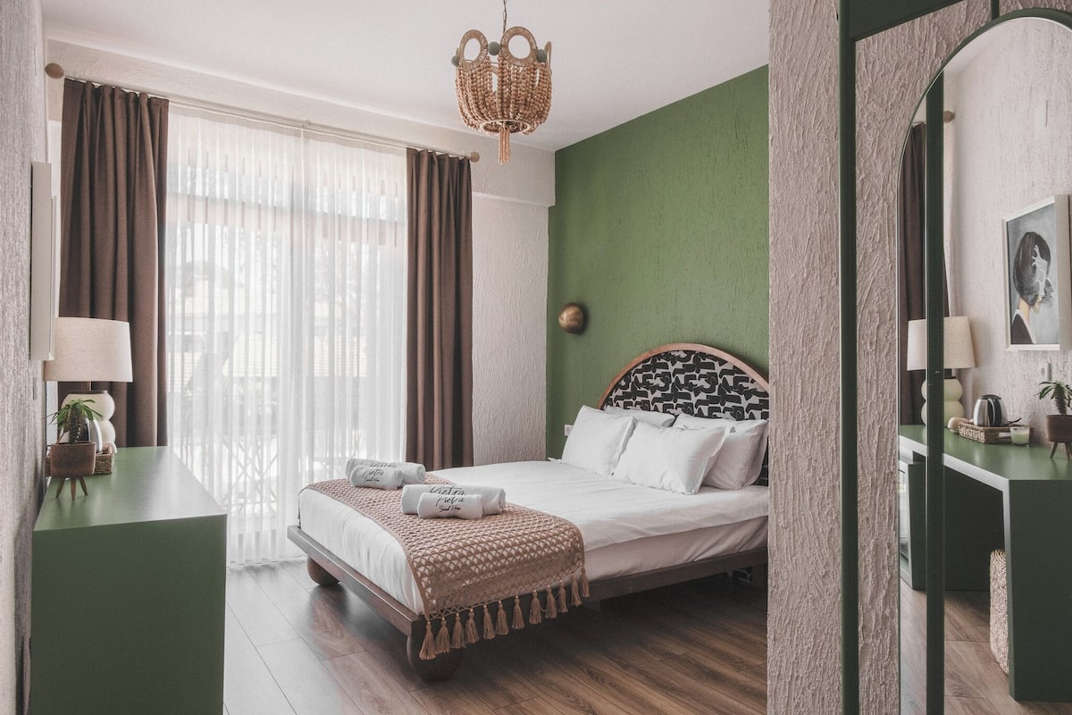 A bedroom with a bed, bedside tables, a mirror, and a window with curtains.