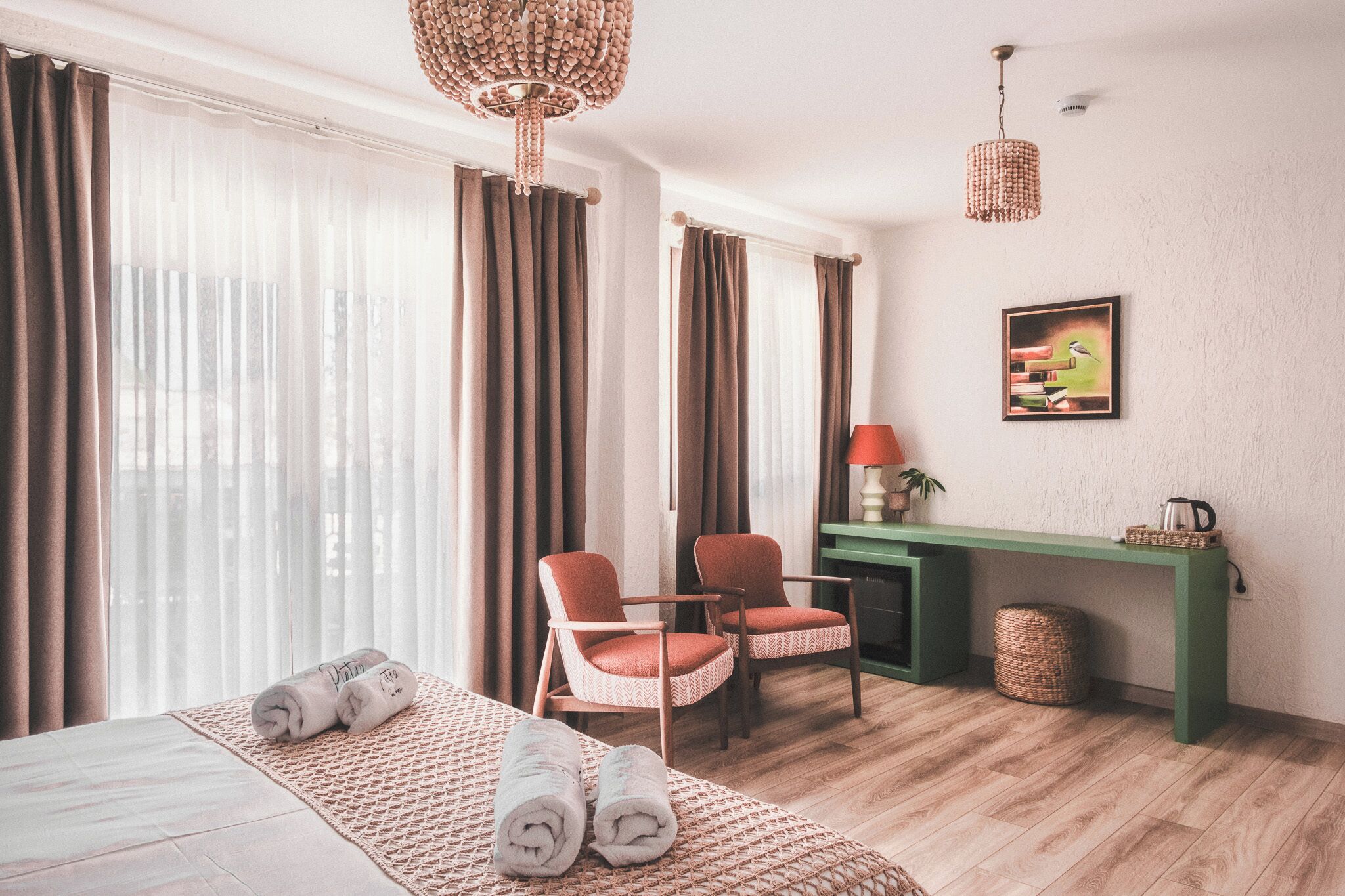 A hotel room with a bed, two chairs, a desk, a lamp, and a painting on the wall.