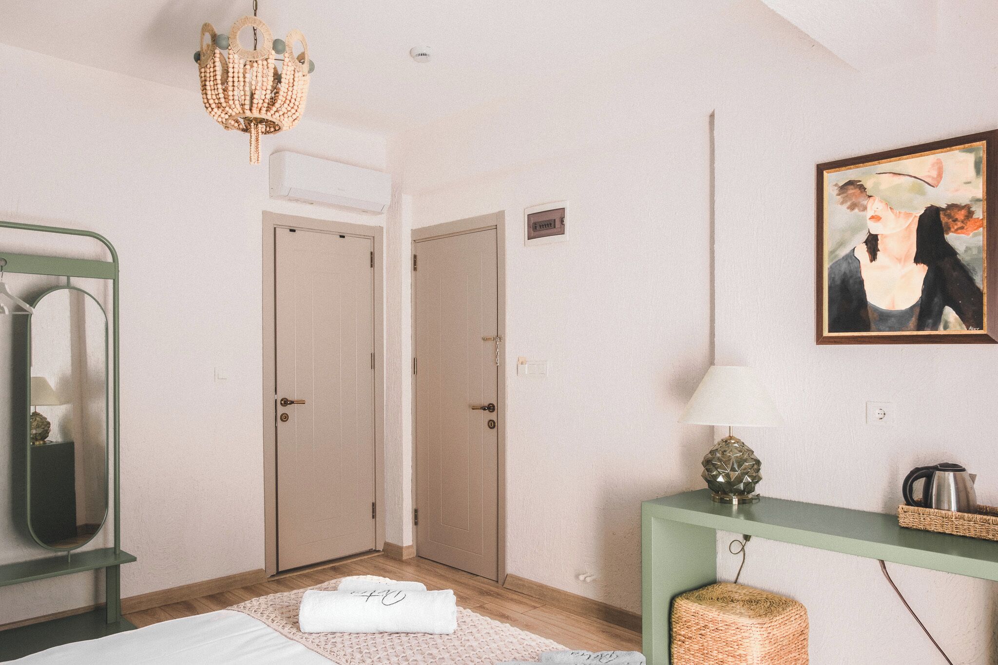 Hotellihuone, jossa on sänky, vihreä konsolipöytä lampun kanssa, taulu ja kattokruunu.