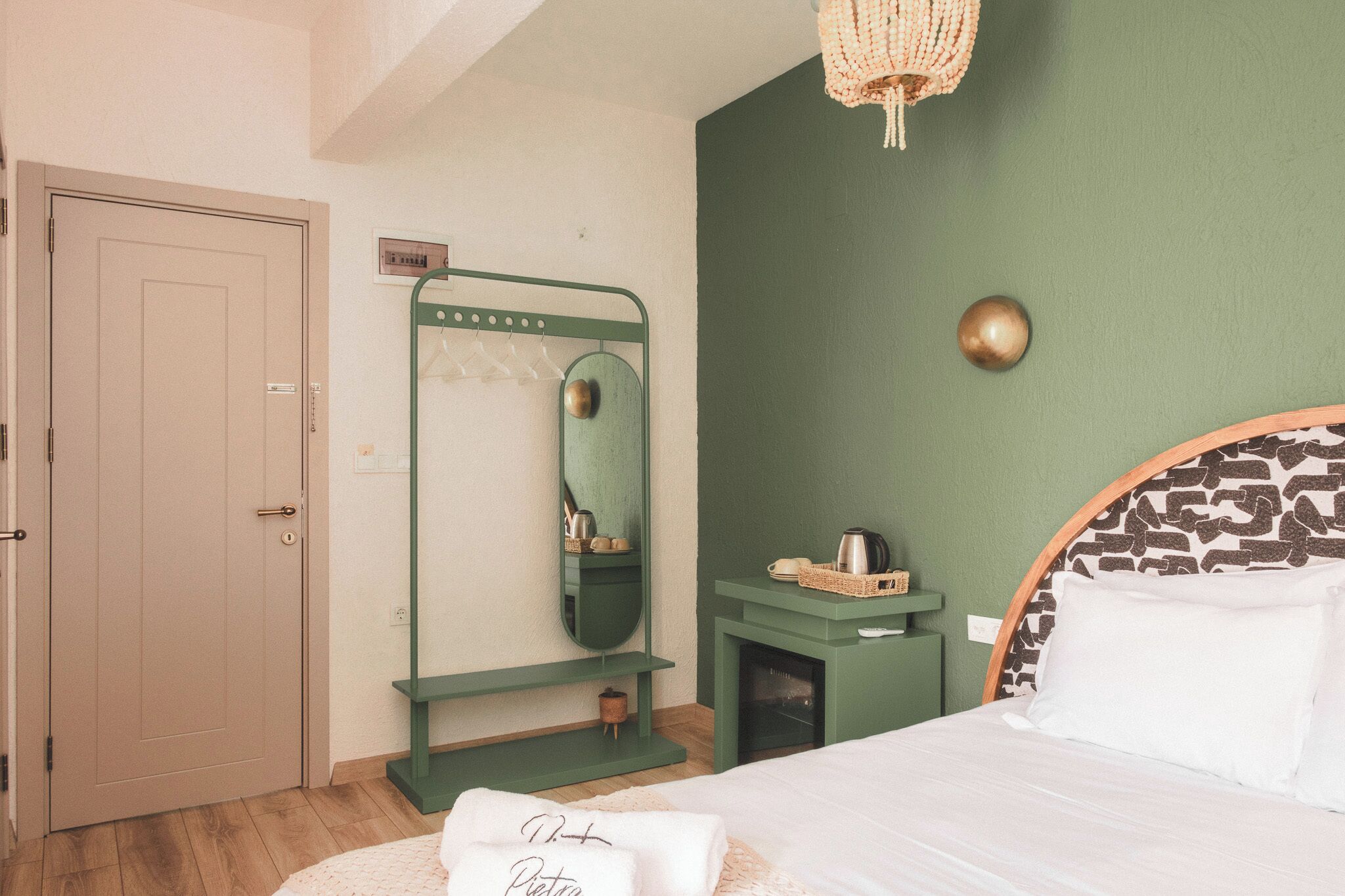 Um quarto com uma cama, parede verde, espelho, prateleira pequena e uma porta.
