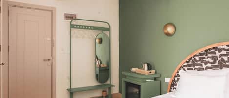 A bedroom with a bed, a green wall, a mirror, a small shelf, and a door.