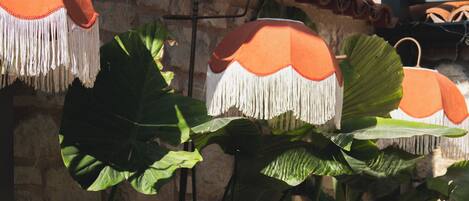 A person seated at a wooden table with a cup and saucer, in a room with large green leaves and orange hanging lamps.