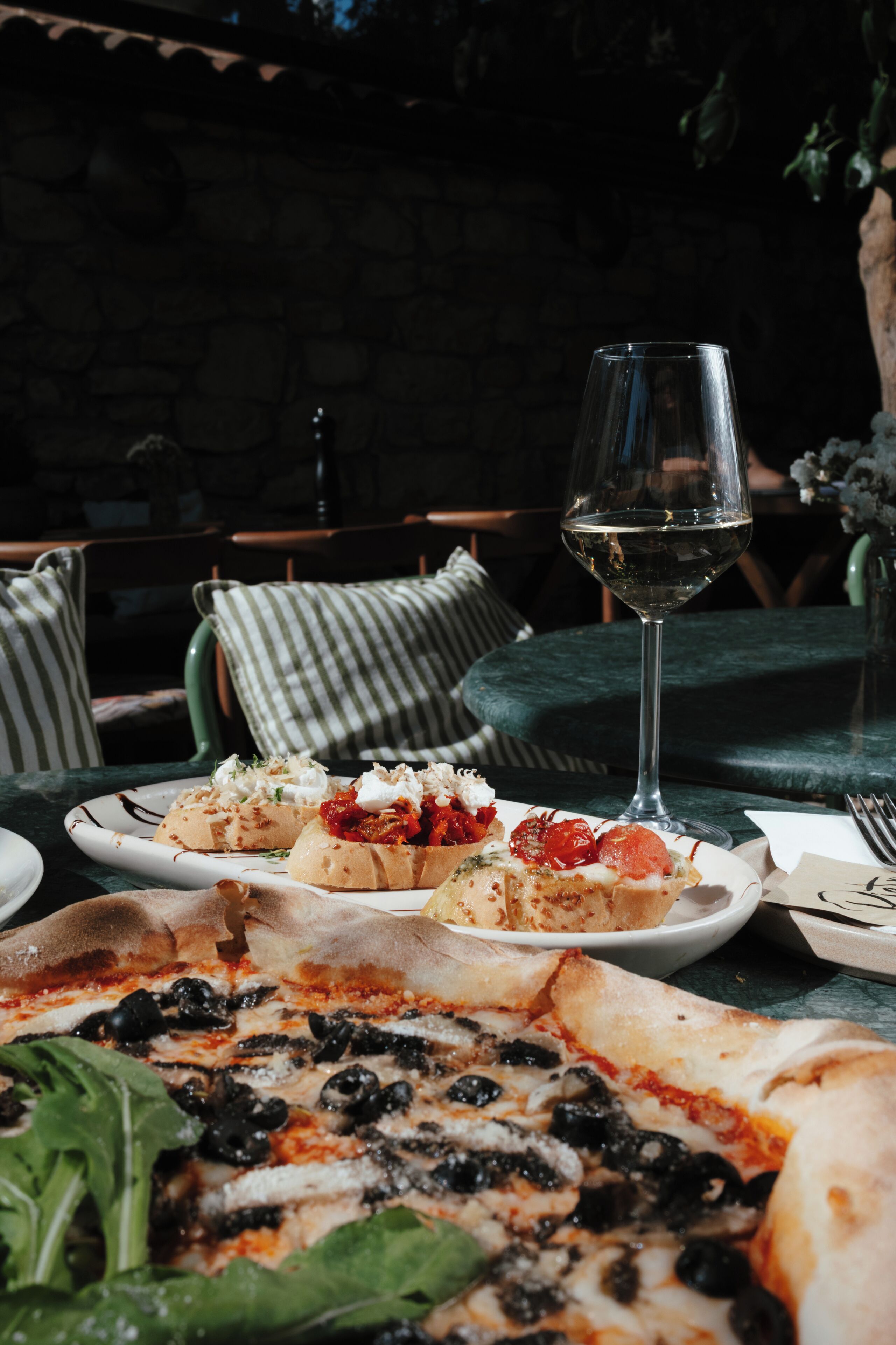 A dining table with a pizza, a glass of white wine, and a plate of bruschetta.
