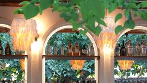 A bar area with wooden shelves stocked with bottles, a green wall, and hanging lights. - Pietra Social House (Urla)