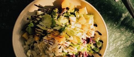 A bowl of salad with a glass of water and a napkin with a fork on a textured surface.