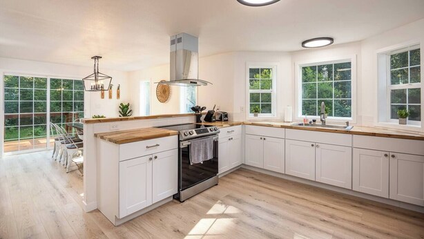 A modern kitchen with white cabinets, a wooden countertop, a built-in oven, and a large window offering a view of greenery. - Updated Large River Front Home with Hot Tub (McKenzie Bridge)