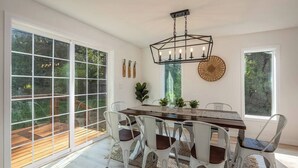 A dining area with a large table, white chairs, and a hanging light fixture. - Updated Large River Front Home with Hot Tub (McKenzie Bridge)
