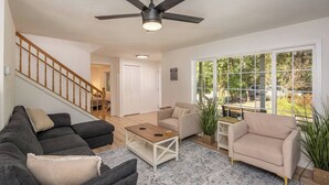 A spacious living room with a ceiling fan, a staircase, and a large window offering a view of the outdoors. - Updated Large River Front Home with Hot Tub (McKenzie Bridge)