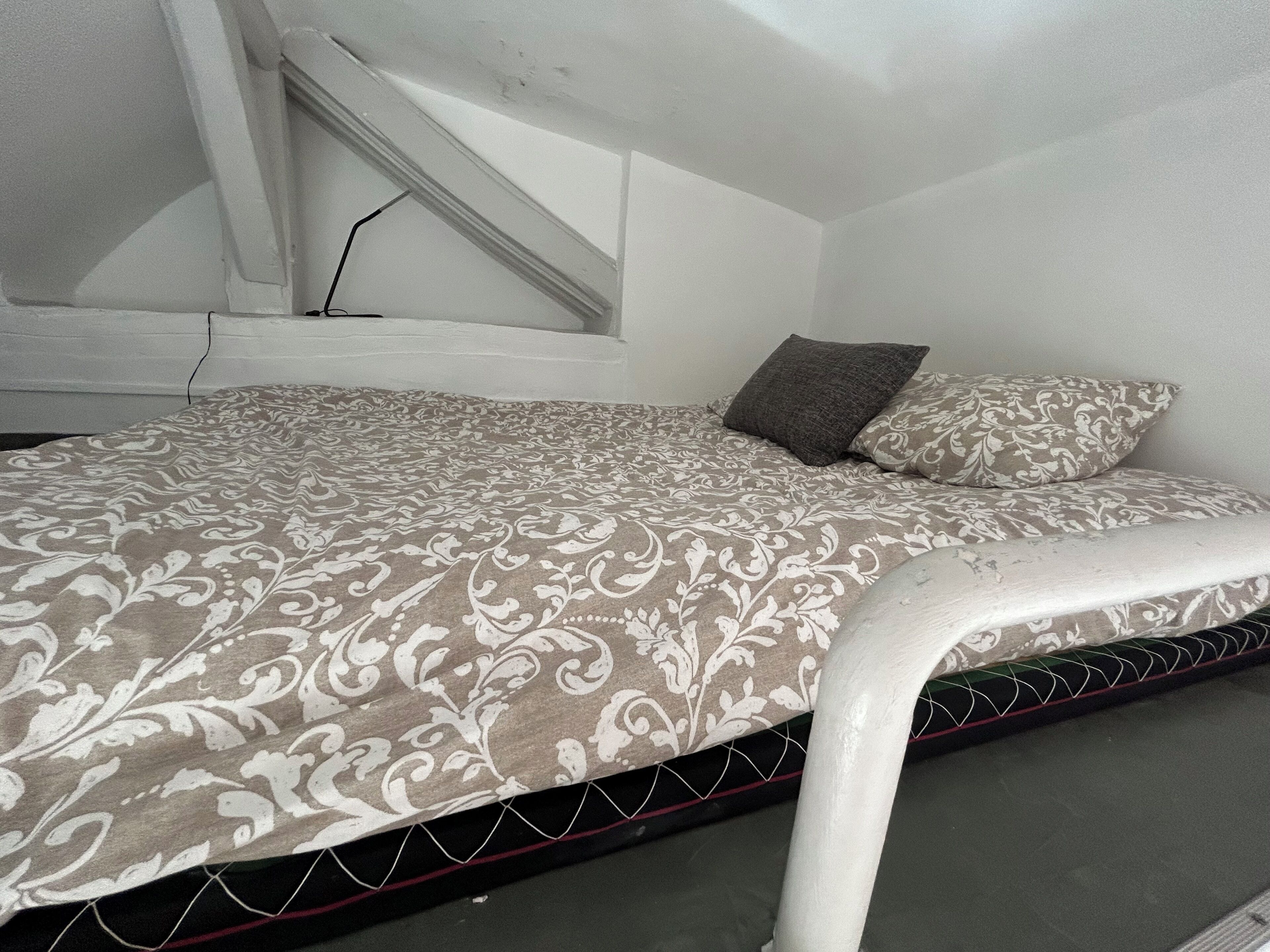 A single bed with a patterned bedspread, a headboard, and two pillows.