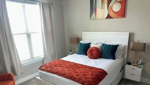 A neatly arranged bedroom with a bed, nightstands, a chair, and a window with curtains.