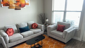 A living room with a grey sofa, a matching armchair, a black coffee table, and a geometric orange rug.