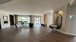 A spacious living area with a large dining table and chairs, a sofa, and a TV mounted on the wall.