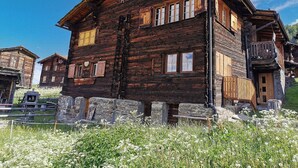 Ein rustikales Holzhaus mit zahlreichen Fenstern und einem Balkon, umgeben von einem Steinfundament und einer grünen Wiese.