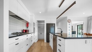A modern kitchen with white cabinets, a black countertop, and a wooden floor. - Beachy Serenity - Waihi Beach Holiday Home (Waihi Beach)