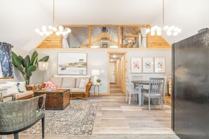 A cozy living room with a wooden ceiling, a dining area with a table and chairs, and a large refrigerator. - NEW-The Beach Haus- Luxe Cottage, professionally designed w/ WiFi, linens incl. (Supply)