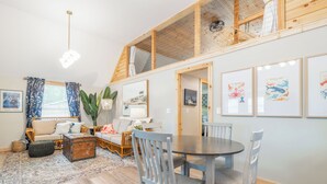 Un salón acogedor con techo alto, vigas de madera, una mesa de comedor y un sofá.