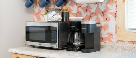 A kitchen with a microwave, coffee maker, and a jar of marshmallows on the counter.